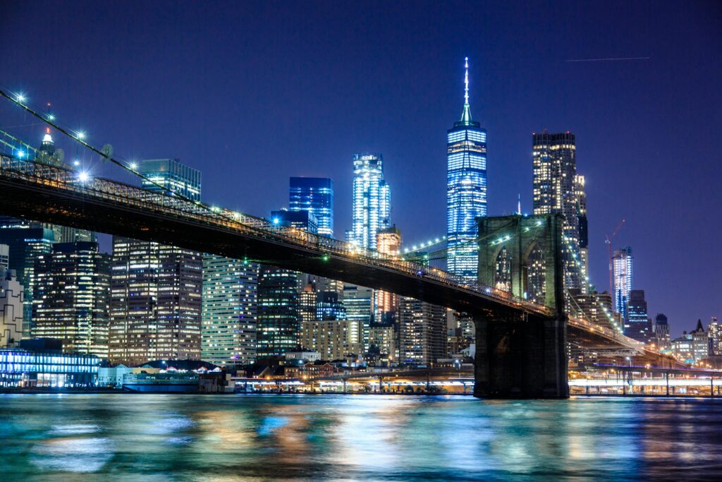 A breathtaking nighttime skyline of New York City, with the Brooklyn Bridge and towering skyscrapers illuminated against the dark sky.