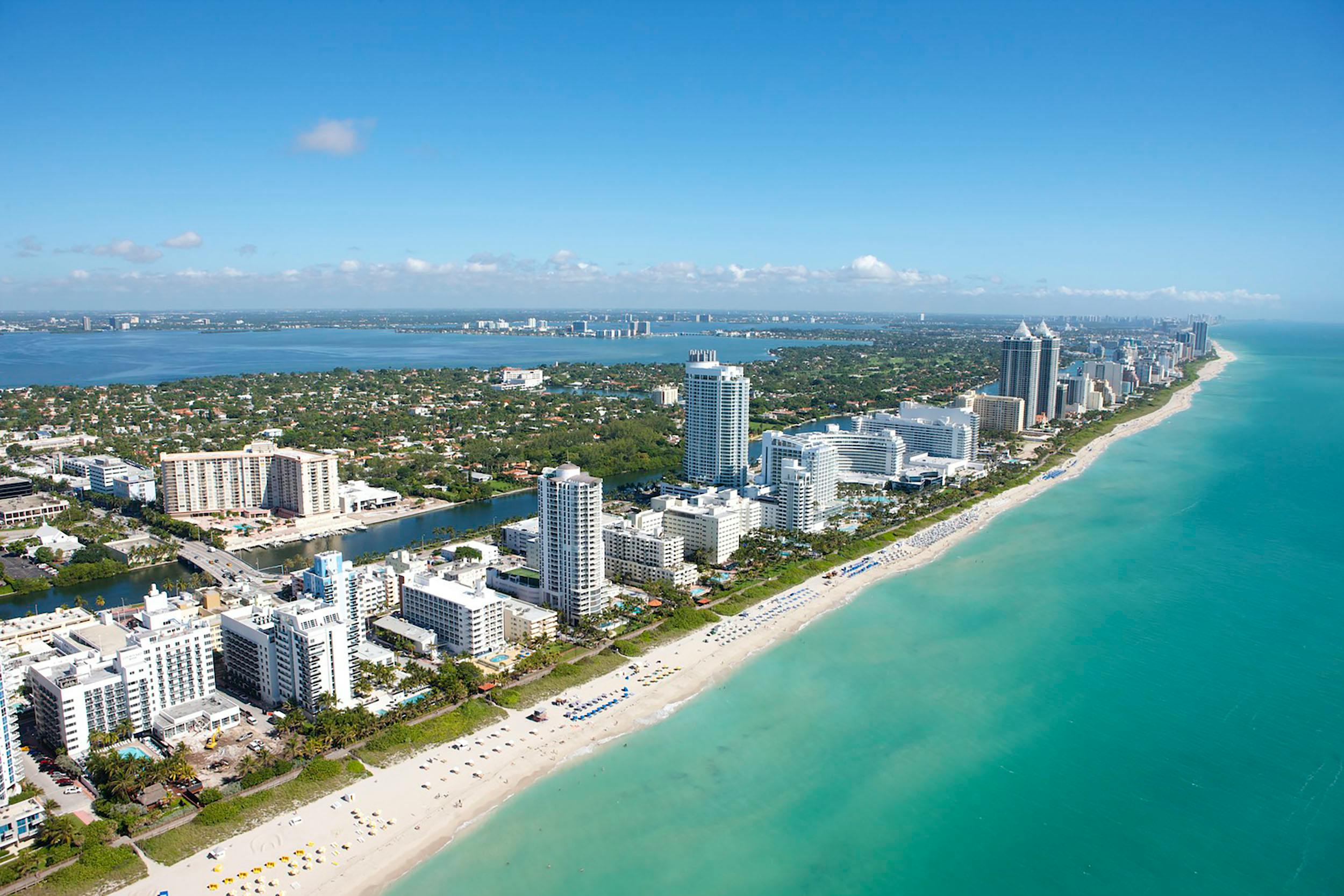 A serene coastal landscape with a rocky shoreline, calm turquoise waters, and a clear blue sky. The scene captures the natural beauty of a quiet beach with scattered rocks and gentle waves. Miami